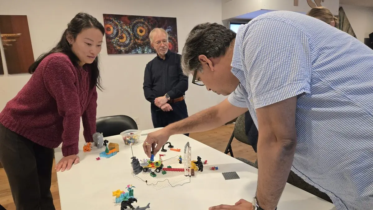 Participants leaning over a shared LEGO Serious Play landscape build during the November 2025 Vancouver cohort